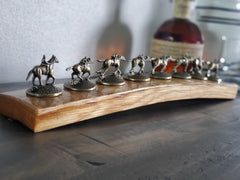 Close-up of horse-and-jockey bottle stoppers displayed on a curved bourbon barrel stave.