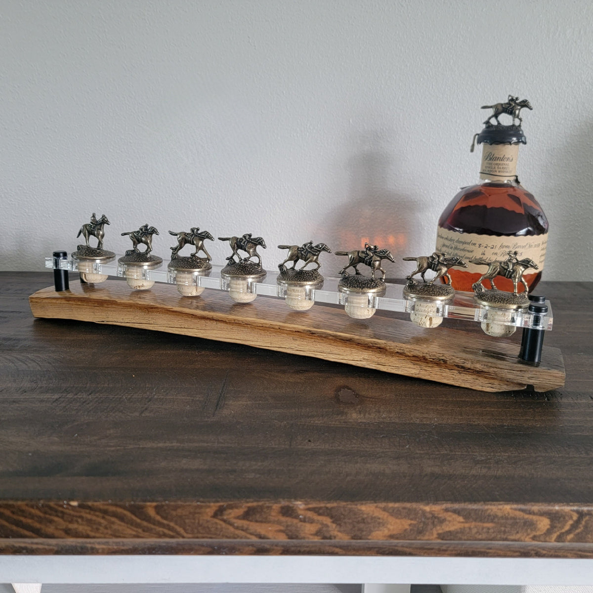 Blanton’s bottle stoppers in a straight row on a barrel-stave display with a clear acrylic platform
